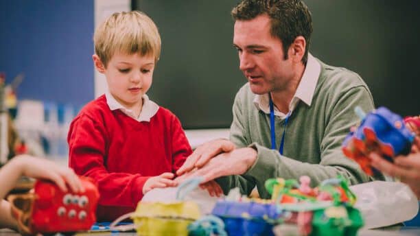 Teacher is helping his primary school student in the classroom with their project.
