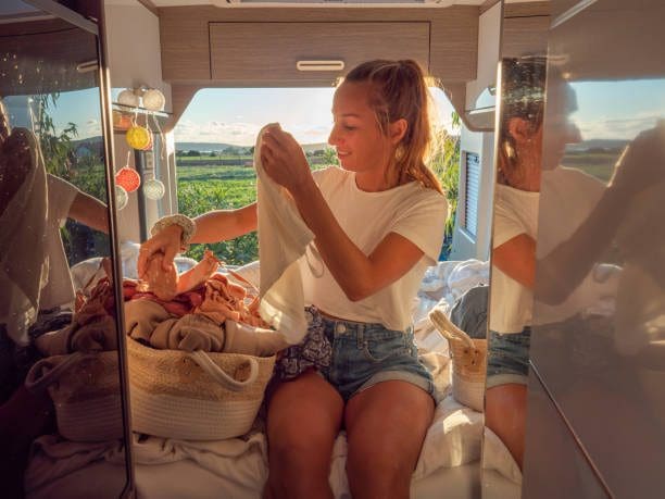 Road trip concept, woman living the van life experience. She prepares the dirty cloths to wash at the back of her camper