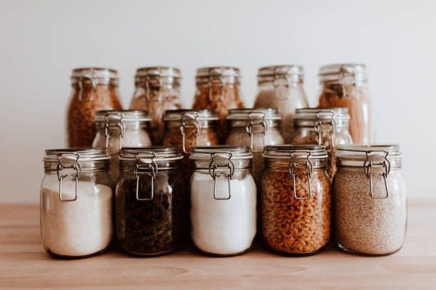 Organized food containers on wooden table in front of a white background. Different type of dried, uncooked ingredients in air tight containers.