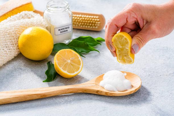 Natural and eco friendly home cleaning products: hand squeezing lemon on a spoon filled with baking soda.