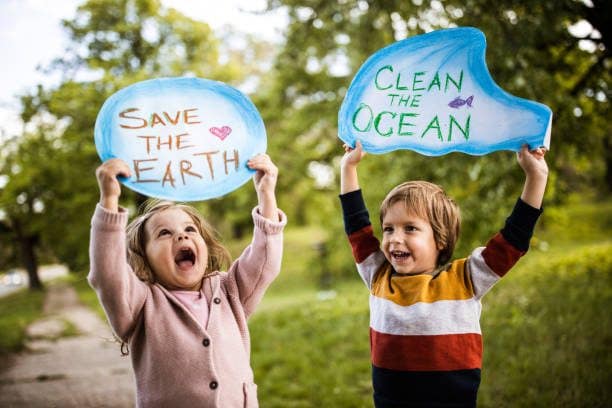 Happy kids holding placards for environmental conservation at the park.