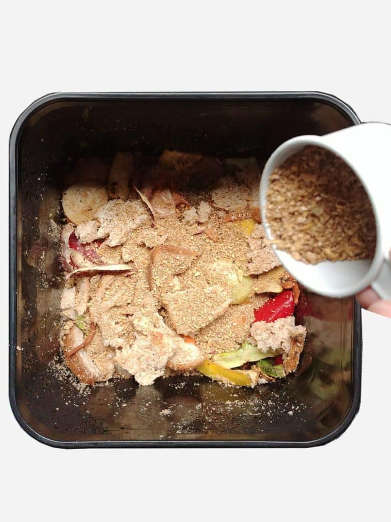 Food scraps inside a Bokashi being sprinkled with powder from a cup